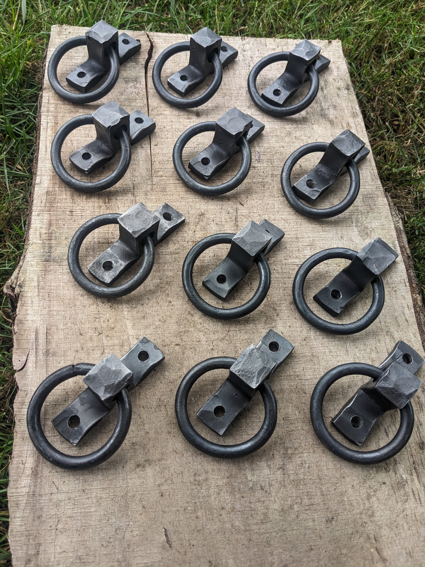Twelve small hand forged ring handles are displayed in a square shape on a live edge board.