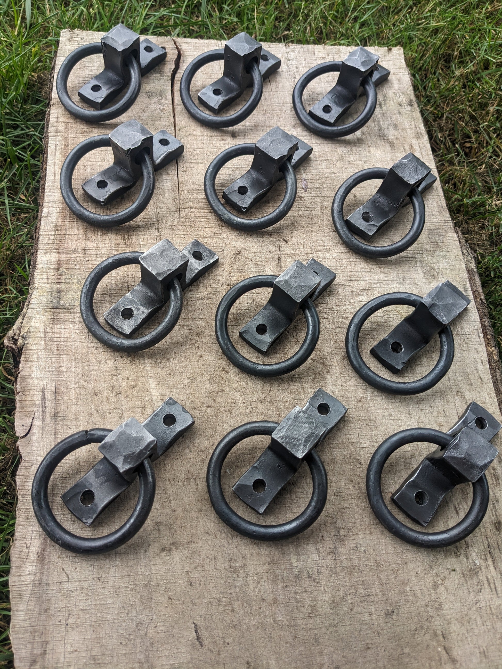 Twelve small hand forged ring handles are displayed in a square shape on a live edge board.