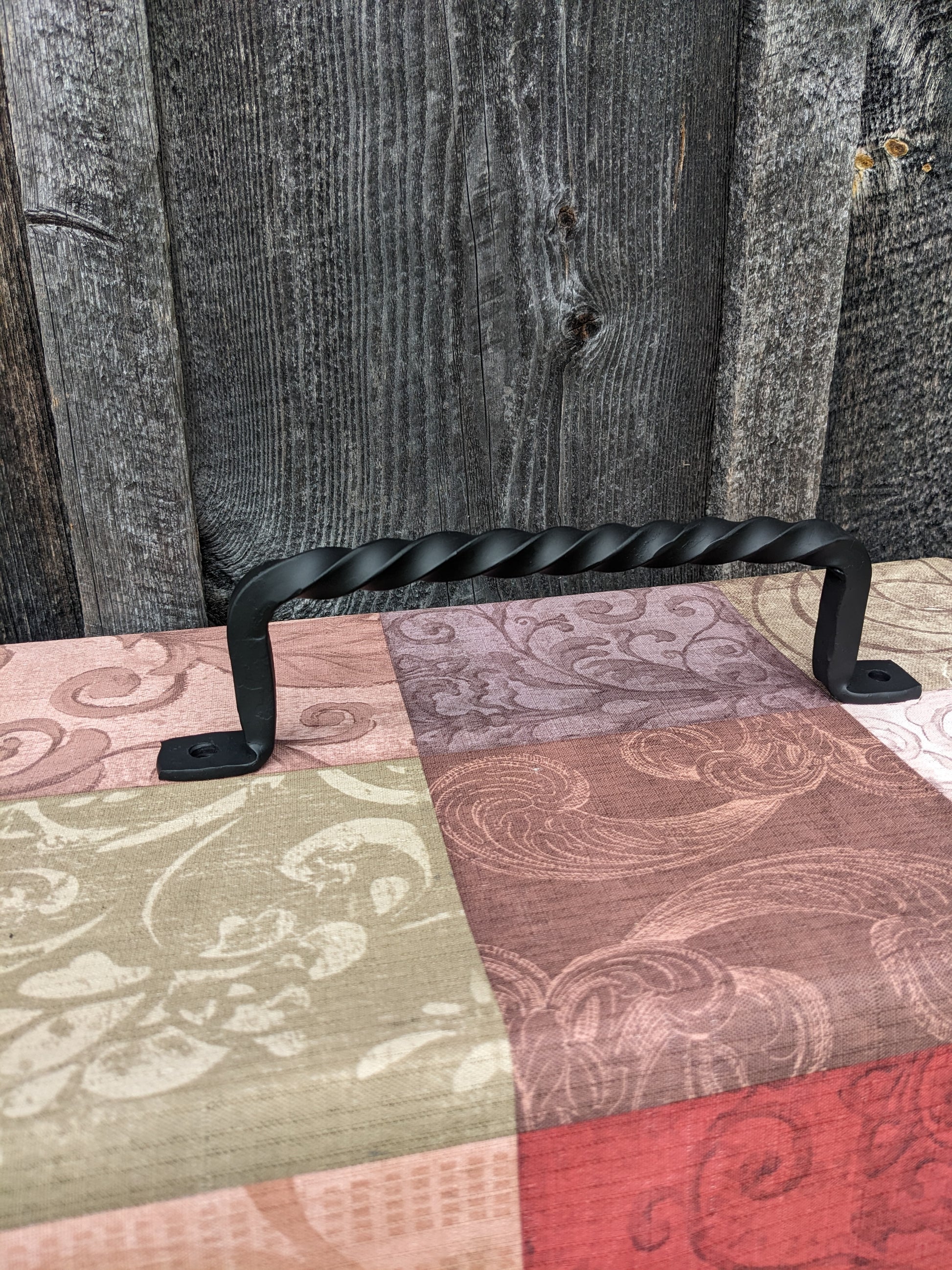 Blacksmith Made twisted handle made of 1/2"  steel sitting on a colorful tablecloth in front of a barn wood wall.