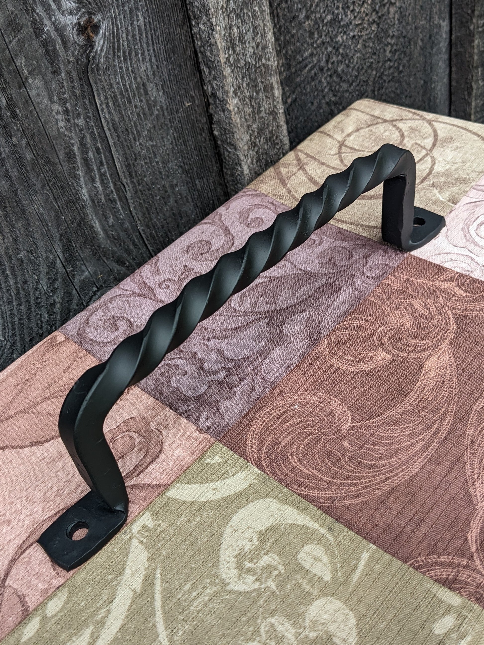 Blacksmith made 11" twisted handle shown at an angle sitting on a colorful tablecloth in front of a barn wood wall