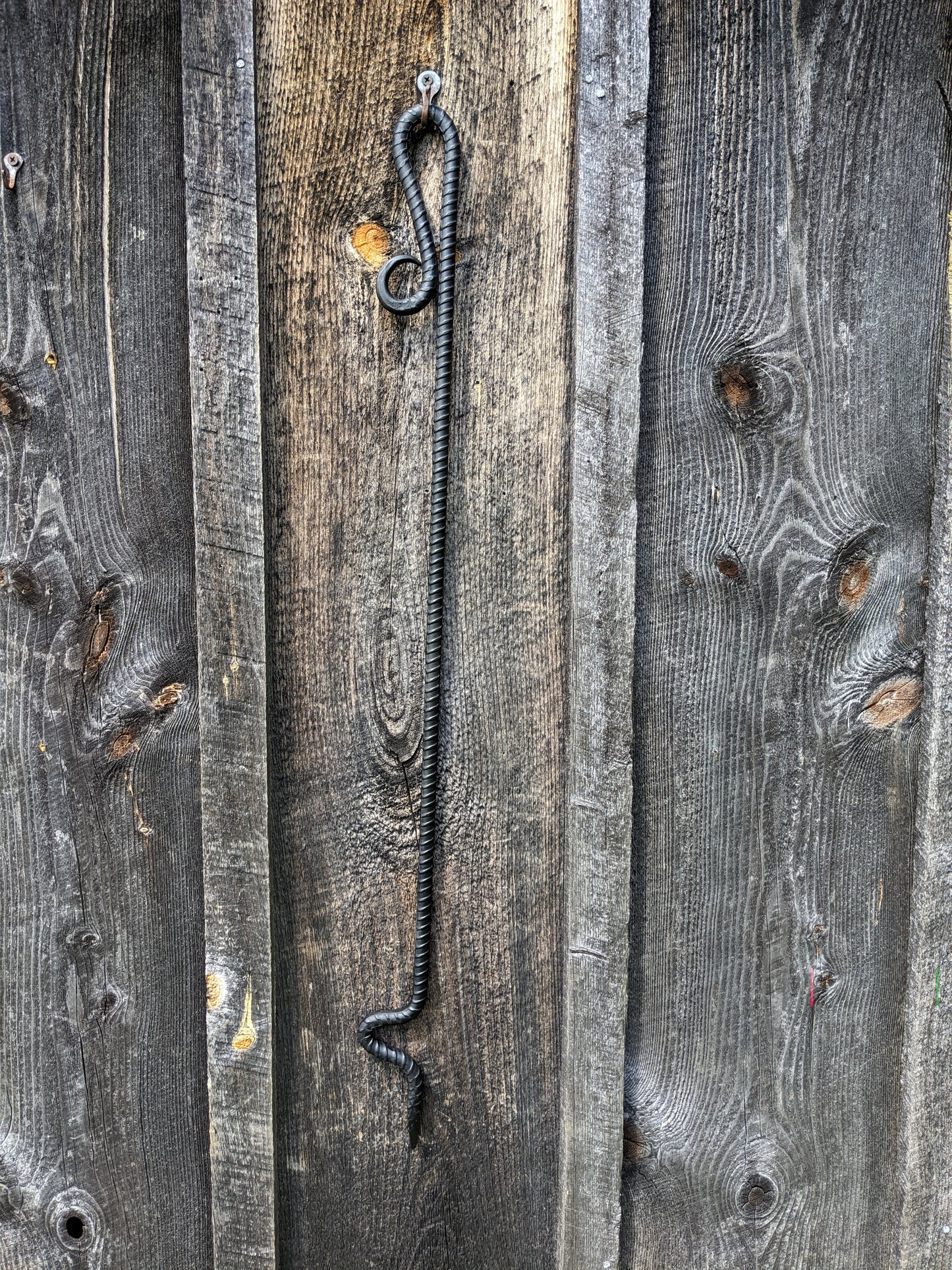 Fire poker made from a single piece of rebar with a scroll handle and curved end for moving wood in your fire. Shown hung on a barn wood wall.