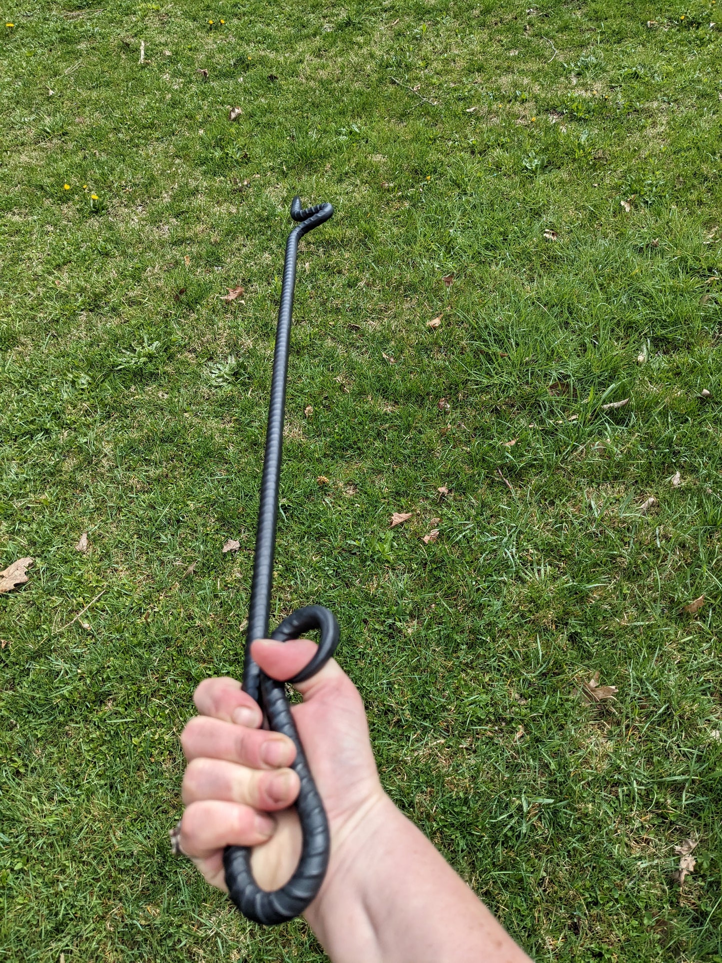 Fire poker made by a blacksmith from a single piece of recycled rebar. Shown being held with a background of grass.