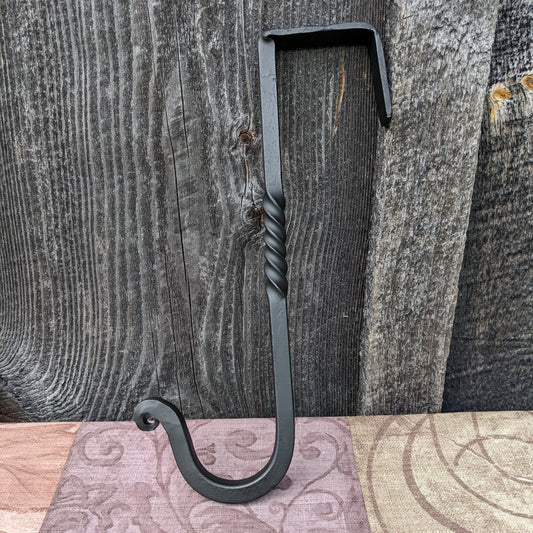 Hand forged hook with a bracket at top to be hung over a door without using screws.  Shown against a barn wood background.