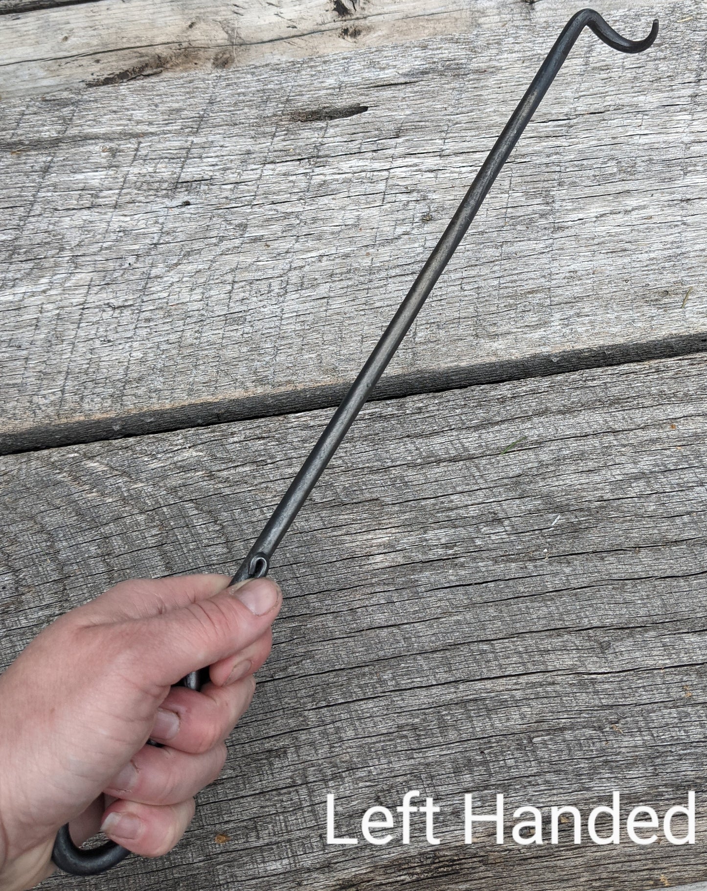 Left handed hand forged steak turner made by a blacksmith. Shown being held infront of a barn wood background.