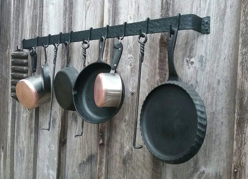 Hand forged hammer finish pot rack made by a blacksmith. 48" long, made of 2" wide steel.has 10 movable hooks. shown holding cast iron pans and stainless steel pots.