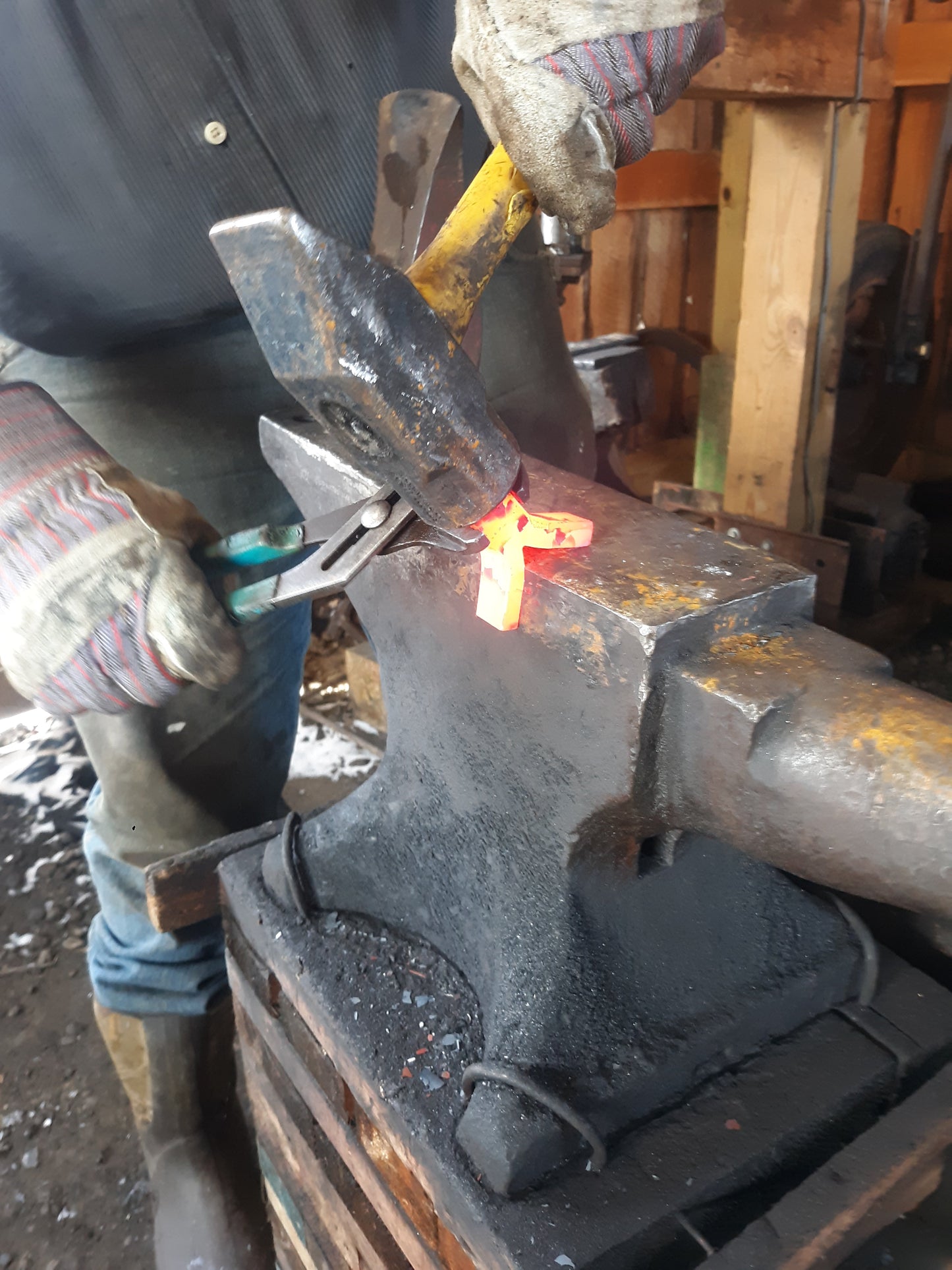 Our blacksmith shapes a red hot piece of metal with a large hammer and anvil. This will become a bracket for one of our hand forged ring handles.