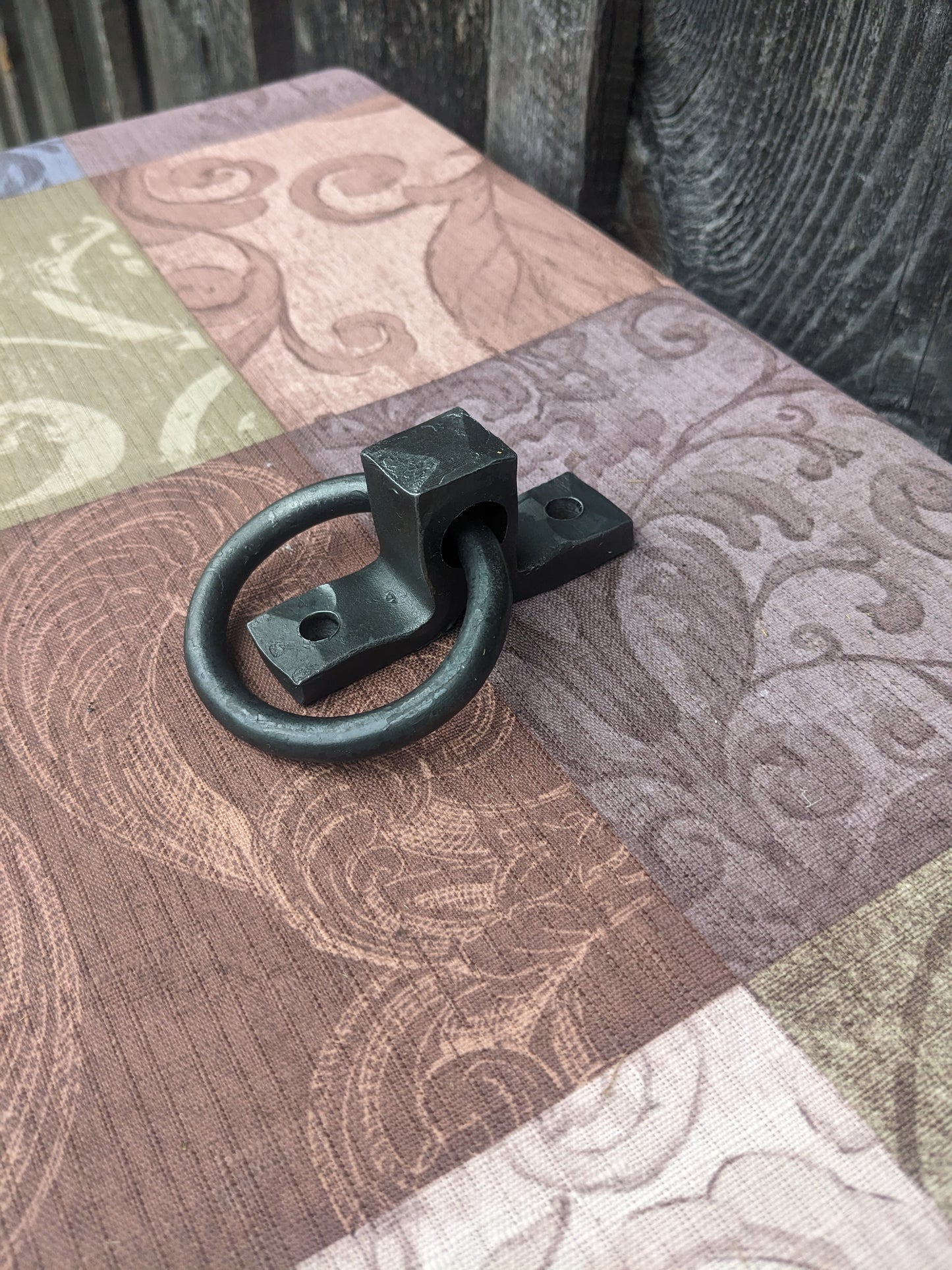 Small hand forged ring handle sitting on a colorful tablecloth in front of a barn wood background.