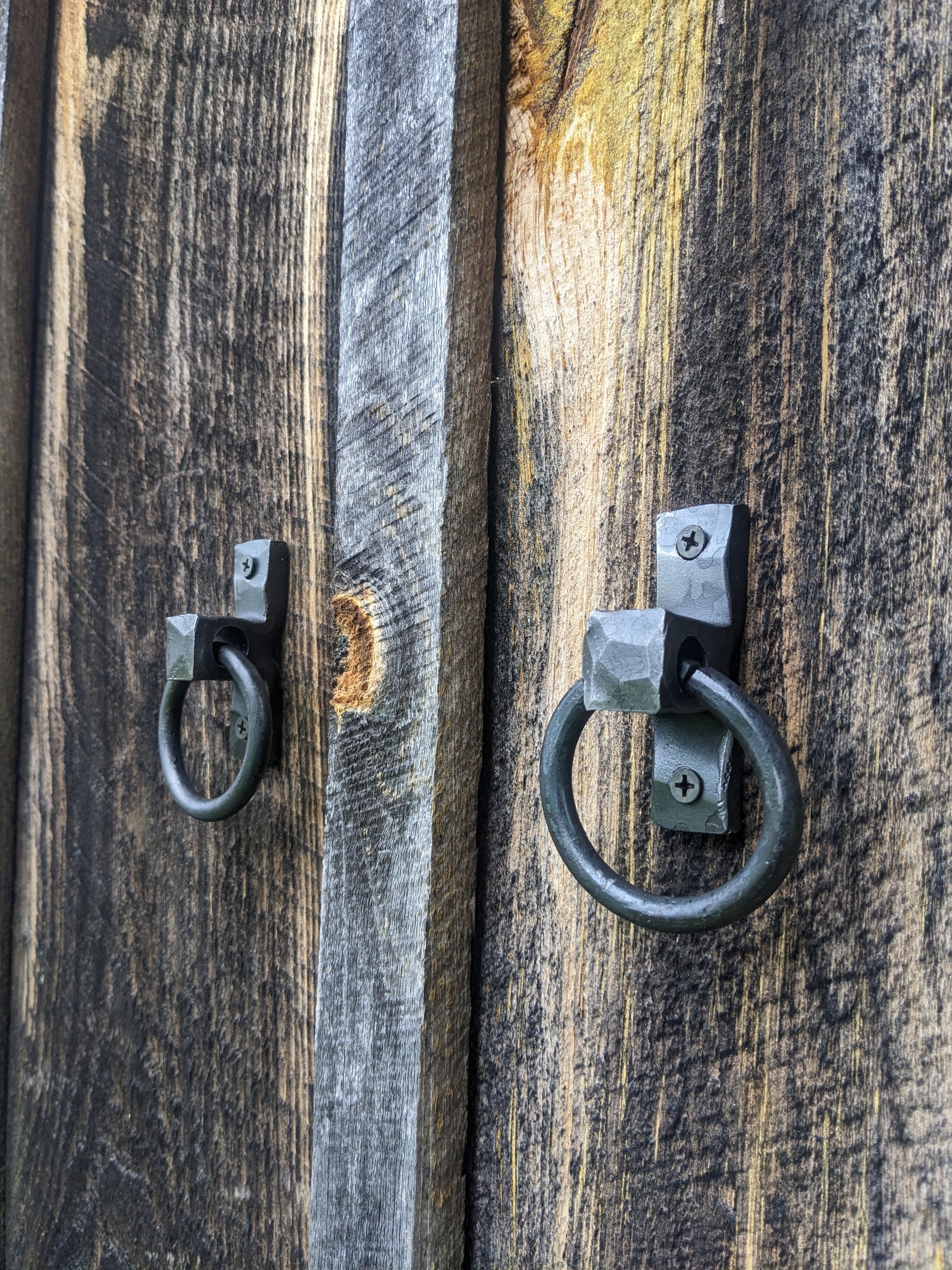 Two small hand forged blacksmith made ring handles mounted onto barn wood doors.