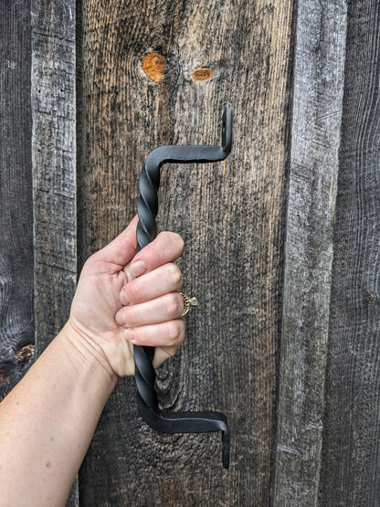 A woman's hand holding a blacksmith made twisted handle to show size in front of a barn wood wall