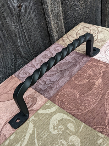 Blacksmith made 11" twisted handle shown at an angle sitting on a colorful tablecloth in front of a barn wood wall 