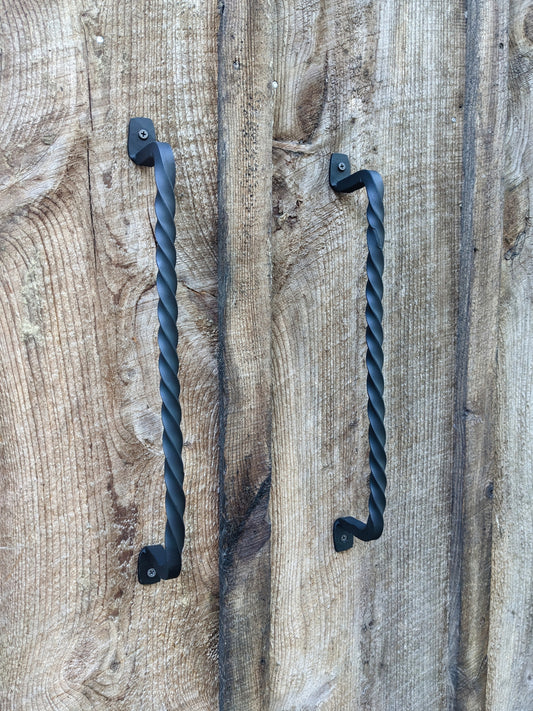 A pair of hand forged twisted handles made by a blacksmith, shown mounted on barn wood doors 