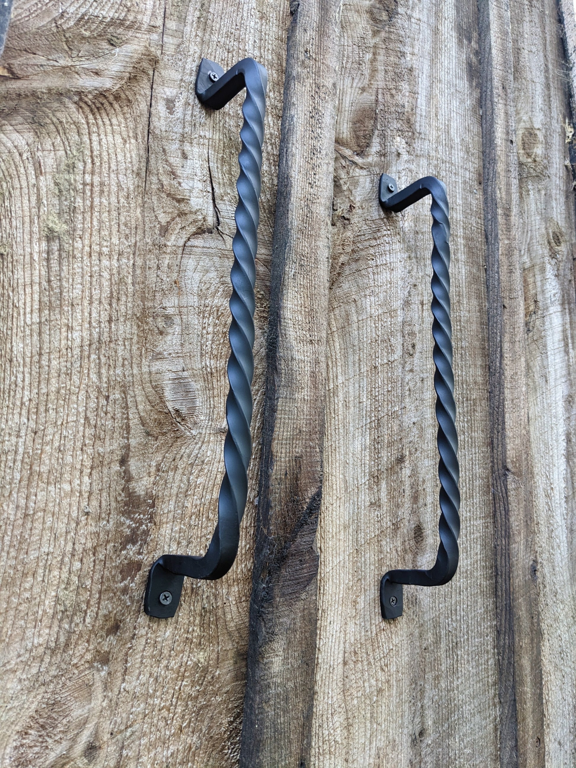 Two hand forged handles, each made of a solid piece of steel hand twisted by a real blacksmith. the view is from underneath looking up and shows the black handles mounted to barn wood doors.