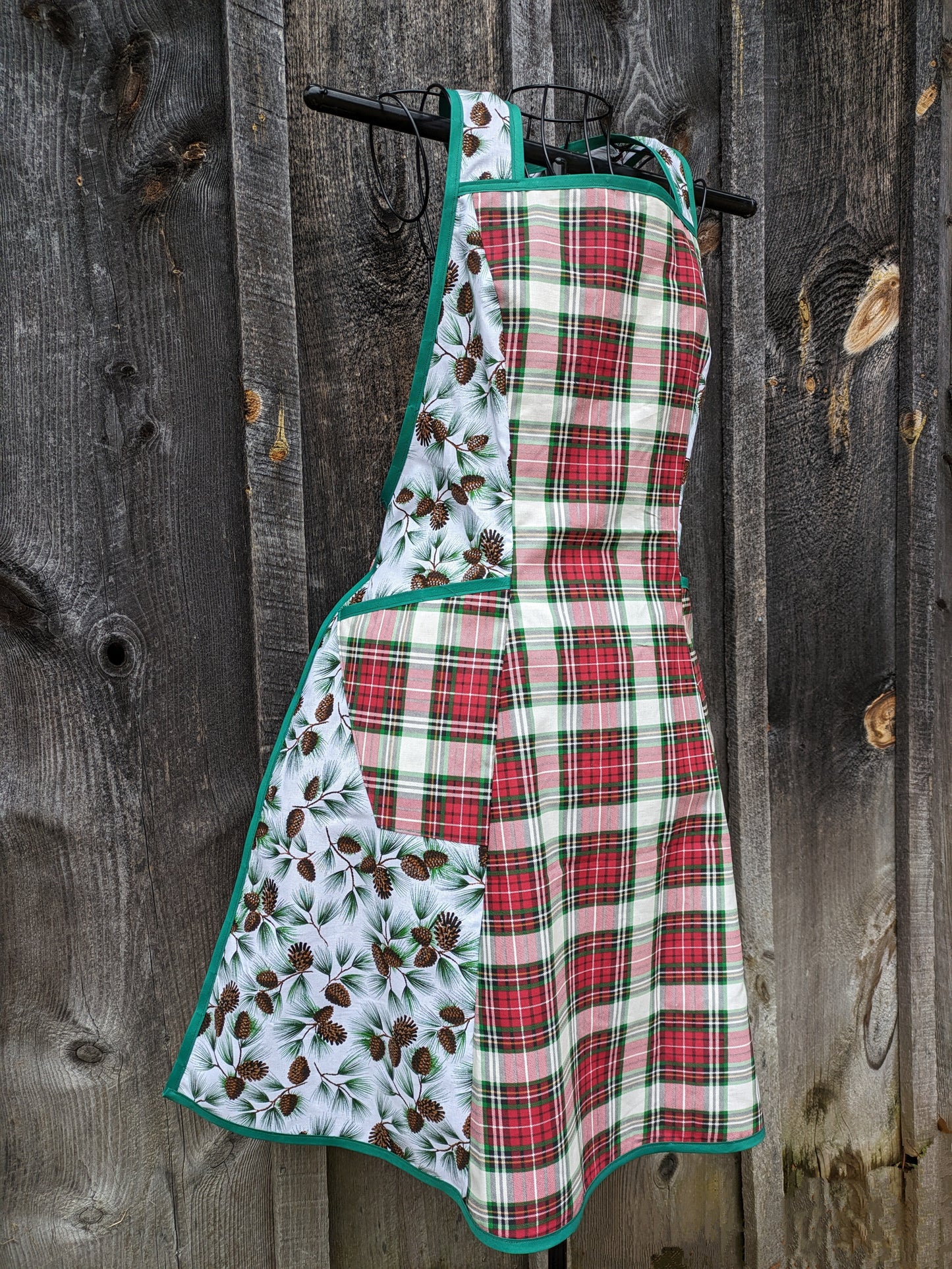 Festive holiday apron featuring a front panel of red and green plaid and sides of glittery pine fabric. Has two pockets and ties in back 