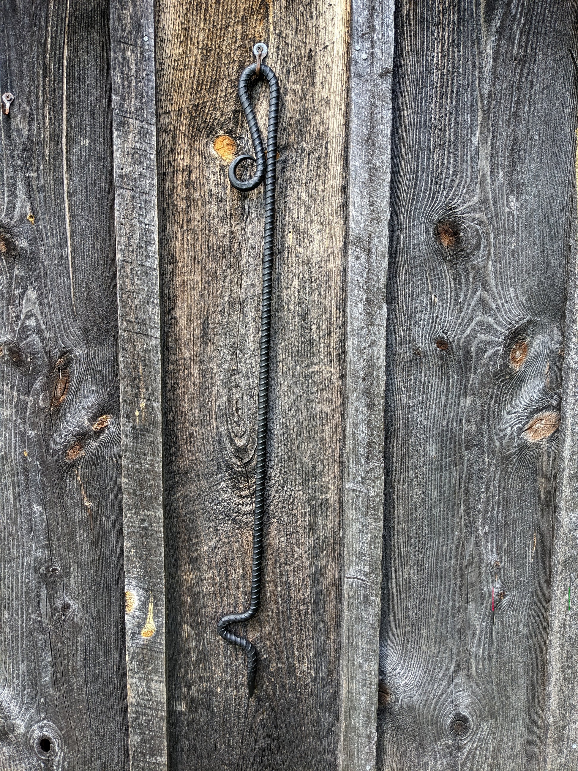 Fire poker made from a single piece of rebar with a scroll handle and curved end for moving wood in your fire.  Shown hung on a barn wood wall.