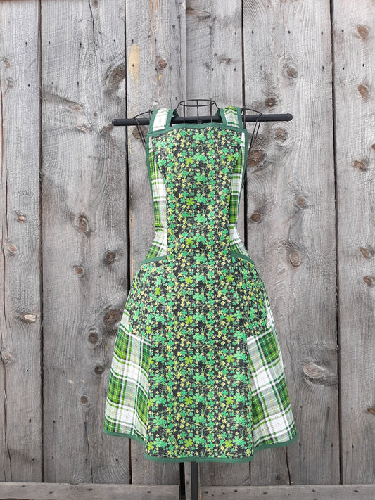 An apron mde from  vintage pattern with prints of green shamrocks on a black background plus green plaid.  