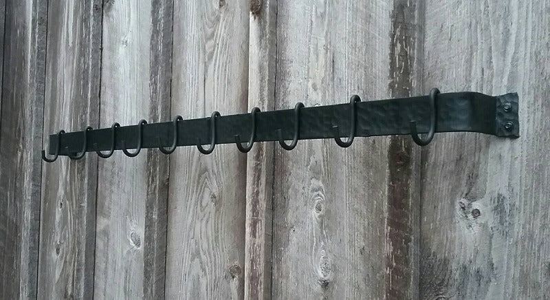 Angeld view of 48" hand forged hammer finish pot rack with 10 movable hooks.  Hooks are empty.  Wrought iron style made by a blacksmith.  Mounted on a barn wood wall.